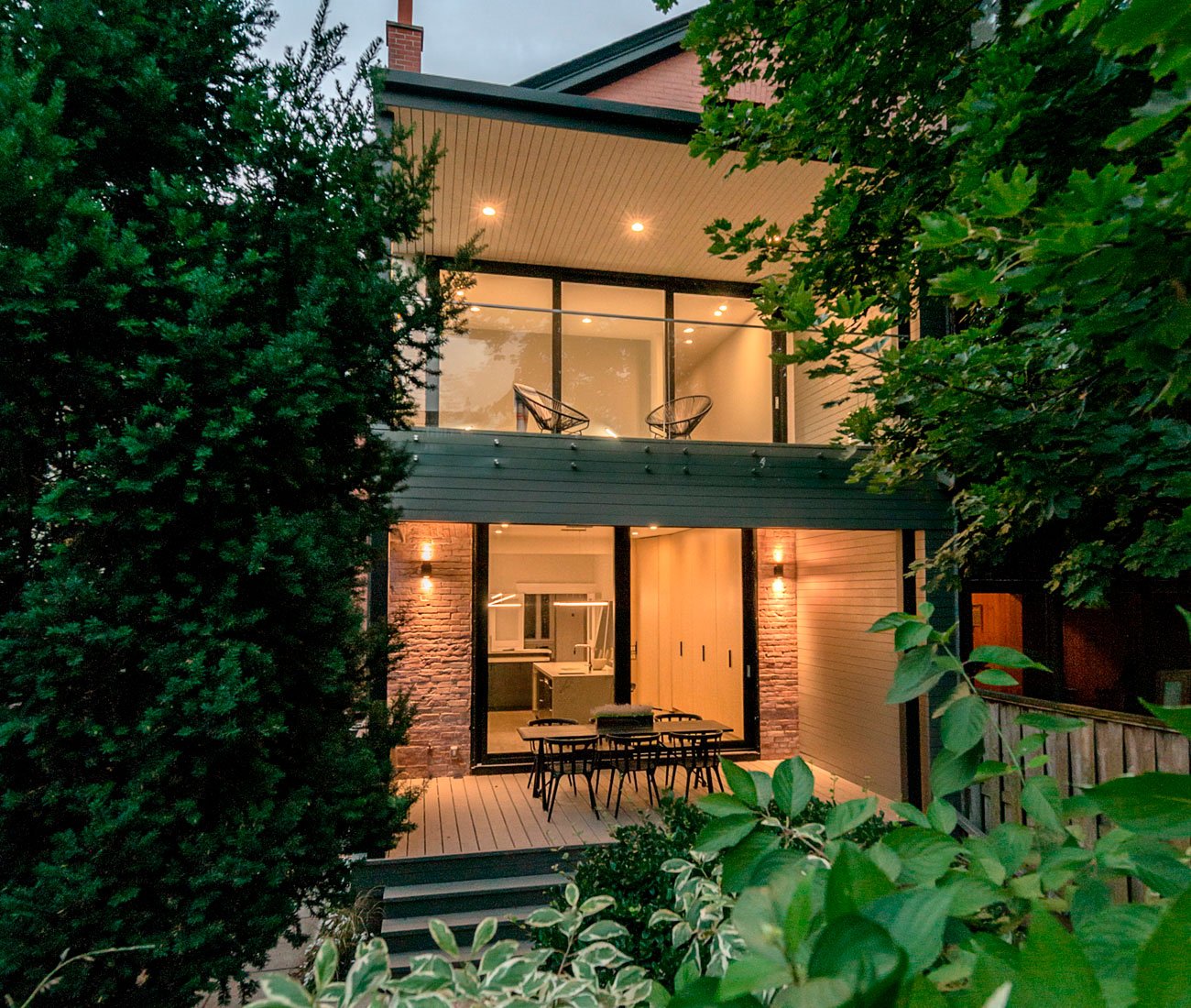 Modern backyard patio with lush tree cover and large glass doors, blending contemporary design with an 1892 Victorian home.