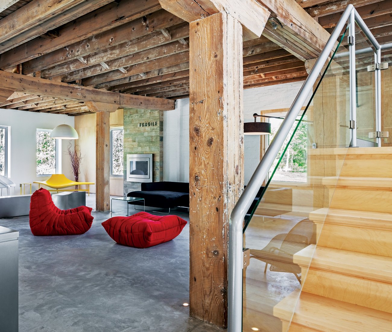 An open stairway leads to the upper level, showcasing a blend of modern interior design and exposed industrial wood beams.